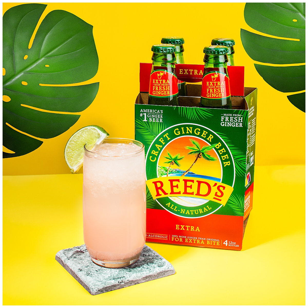A tall pink cocktail with ice and a lime sits on a stone coaster next to a four-pack of unopened bottles of Reed's Craft Ginger Beer. They're sitting on a yellow background with monstera leaves behind them. The cocktail is also made with ginger ale.