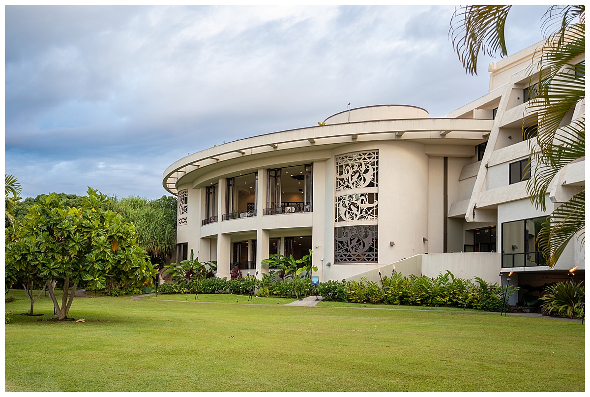 The outside of the resort. The building is white and circular with lots of windows. There is a big green lawn in front with lots of plants.