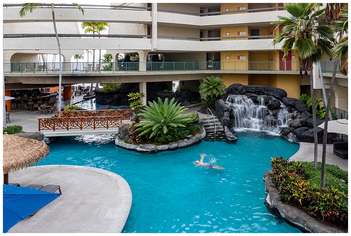 A view of the adults only pool. A man is swimming and there is a rock waterfall feature in the corner.