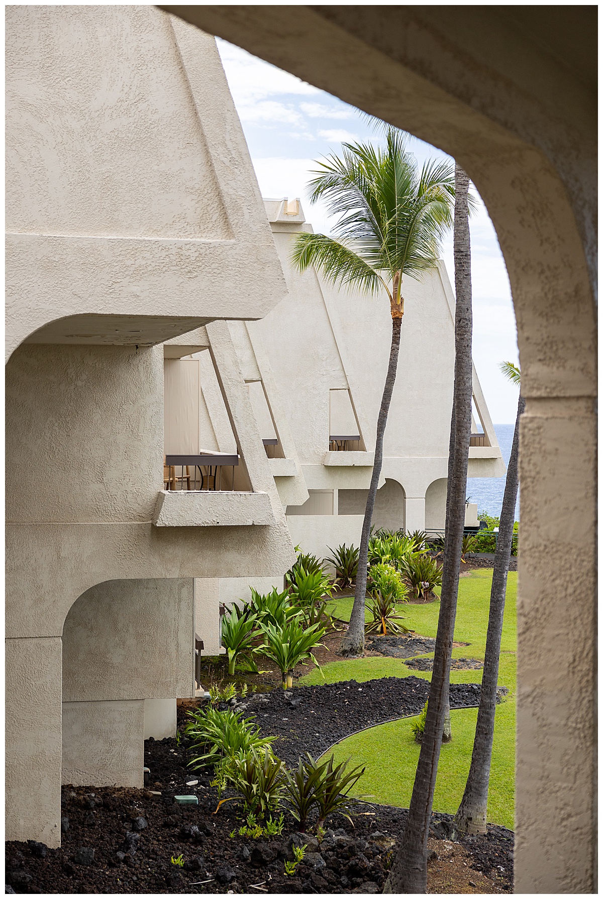 The side of the building. The rooms' lanais jut out over the lawn in a triangular shape. There is lots of plants and greenery.